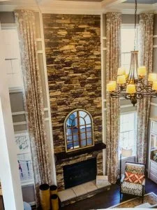 Tall cultured stone fireplace wall with arched window and chandelier in East Brunswick, NJ by CMB Stucco