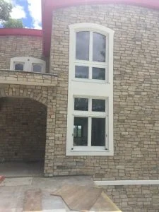 Custom home exterior with stone veneer walls and tall arched window in East Brunswick, NJ by CMB Stucco